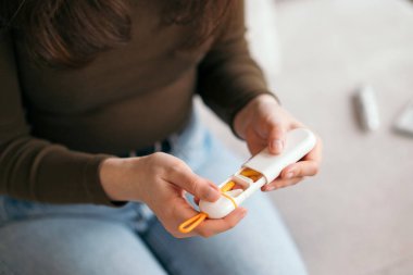  Kanepede oturmuş evde günlük ilaç hazırlarken elinde bir hap organizatörü tutan kadın. 