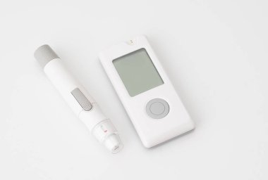 Beyaz zemin üzerinde kan şekeri ölçer ve tükenmez kalem, diyabet izleme ve kan şekeri testlerinde kullanılır. 