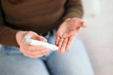 Genç bir kadın evdeki kan şekerini glukometreyle ölçüyor, diyabet hastalığını kanepede izliyor. 