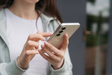 El ele tutuşmak ve modern bir akıllı telefonu açık havada kullanmak, günlük hayatta teknolojiyi ve bağlantıyı göstermek..