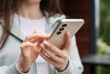 El ele tutuşmak ve modern bir akıllı telefonu açık havada kullanmak, günlük hayatta teknolojiyi ve bağlantıyı göstermek..