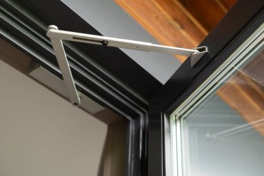 Açık alüminyum çerçeveli penceredeki modern bir pencere menteşesinin yakın çekimi, yapım detaylarını ve mühendislik tasarımı.