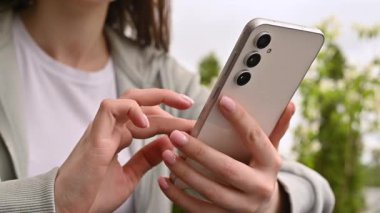 El ele tutuşmak ve modern bir akıllı telefonu açık havada kullanmak, günlük hayatta teknolojiyi ve bağlantıyı göstermek..