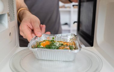 İnsan, ısıtmak için alüminyum tepside hazır yemeği mikrodalga fırına koyar. 