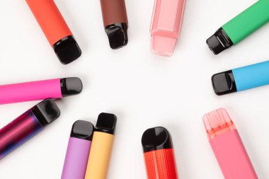Beyaz arka planda daire şeklinde dizilmiş çeşitli renkli tek kullanımlık kalemler, modern elektronik sigara içme cihazları. Boşluğu kopyala. 