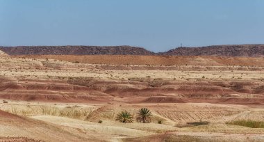 Sahra Çölü 'ndeki turuncu kum tepeleri ve dağlarla dolu, parlak mavi gökyüzü ve Fas' ta bulutlarla dolu resimli bir manzara.