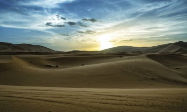 Çöldeki kum tepelerinin üzerinde gün batımı. Sahra Çölü 'nün ıssız manzarası