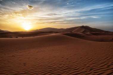 Çöldeki kum tepelerinin üzerinde gün batımı. Sahra Çölü 'nün ıssız manzarası