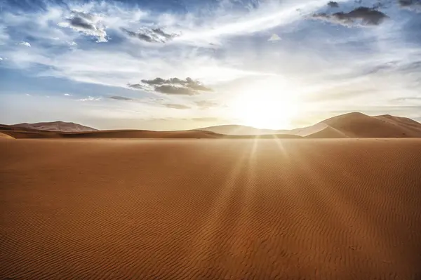 Desert dunes landscape with sun flare on cloudy sky background, Sahara, Morocco