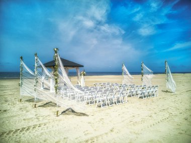 Güzel deniz ve mavi gökyüzünün arka planına karşı sahilde hazırlanmış sunak ve sıra sıra beyaz sandalyeler. Varış yeri düğünü ve tropikal bir ülke konseptinde kutlama.