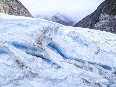 Parts of the fox glacier in New Zealand with deeply hanging clouds and crest. clipart