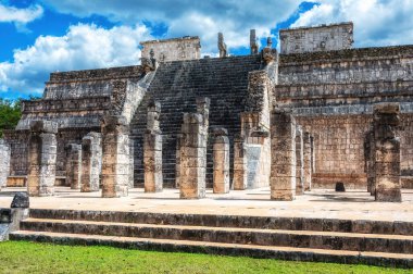 Chichen Itza arkeolojik alanındaki savaşçıların tapınağının manzarası, canlı mavi gökyüzüne karşı antik Maya mimarisini sergiliyor.