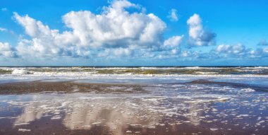 Bu sakin sahil sahnesinde engin bir kumlu sahil manzarası var dramatik mavi gökyüzünün yansımaları ve dağınık bulutlar, yumuşak okyanus dalgalarıyla buluşuyor..