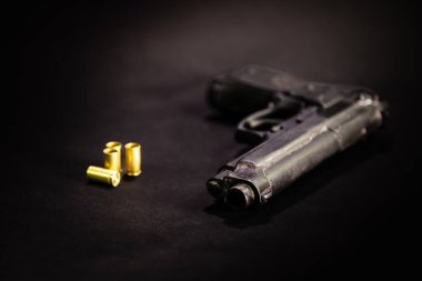 Pistol with 9mm shell casings on black background, macro shot