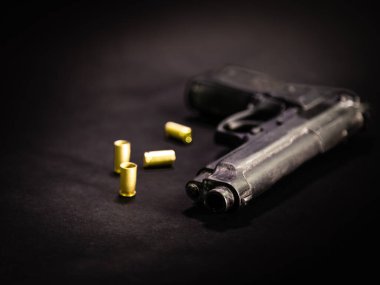 Pistol with 9mm shell casings on black background, macro shot