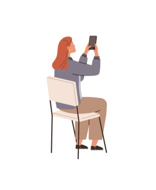 Kızıl saçlı bir kadın bir sandalyede oturuyor ve elinde fotoğraf çekmek için akıllı telefon tutuyor. O, mavi ceket ve kahverengi pantolon giydi. Teknoloji, sosyal medya, iletişim, yaşam tarzı için ideal