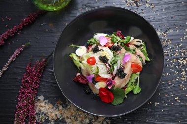 Sebzeli salata, taze balık, havyar ve yenebilir çiçeklerle süslenmiş bıldırcın yumurtası. Siyah kasede balık salatası, üst manzara..