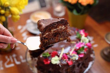 Bir parça çikolatalı pasta, seçici odaklanma, yakın plan, bulanık arka plan. Çikolata jöleli havuçlu kek, krem peynir ve yenebilir çiçeklerle süslenmiş hurmalar, yatay manzara..