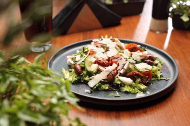 Domatesli salata, peynir, salatalık, zeytin ve balzamik sirke. Siyah tabakta taze sağlıklı bir öğle yemeği, ahşap masada, seçici bir odak..