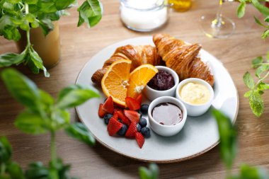 Fransız kahvaltı seti, en iyi manzara. Kruvasan, taze meyve, tereyağı ve reçel, beyaz bir tabakta, seçici bir odak. Restoranda nefis bir kahvaltı.. 