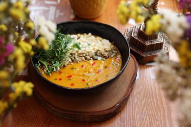 Kremalı balkabağı çorbası, füme süzme peynir, kavrulmuş tohumlar ve taze yeşillikler ile servis edilir, seçici bir odak noktası. Vejetaryen çorbası siyah bir kasede, tahta bir masada, yahudi mutfağında.