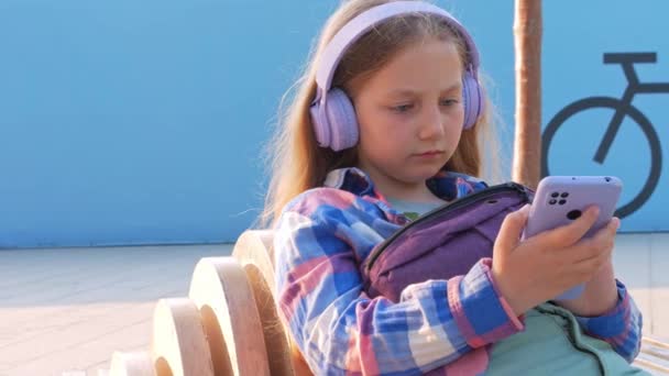 금발의 어린이 헤드폰 검사를 셔츠는 도시의 밖에서 음악이 스마트폰 소리를 — 비디오