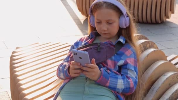 金发儿童耳机格子衬衫听音乐播客智能手机城外的城市街道生活方式 聚精会神的女孩在线有声读物社交媒体4K 心理卫生应用压力缓解应用 — 图库视频影像