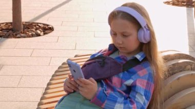 Sarışın çocuk kulaklıkları. Damalı gömlek. Şehir merkezinin dışında müzik podcast akıllı telefon. Konsantre kız çevrimiçi sesli medya 4K. Ruh sağlığı başvurusu Stres destek uygulaması