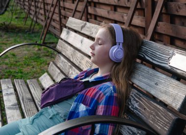 Sarışın çocuk mor kulaklıkları şehir merkezinin dışında meditasyon müzik podcast akıllı telefon kulübesi dinliyor. Konsantre olmuş genç kız sesli kitabı Zihinsel Sağlık Stres Dijital Uygulaması