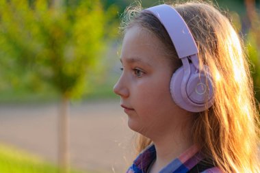 Sarışın çocuk mor kulaklıkları şehir merkezinin dışında meditasyon müzik podcast akıllı telefon kulübesi dinliyor. Konsantre olmuş genç kız sesli kitabı Zihinsel Sağlık Stres Dijital Uygulaması