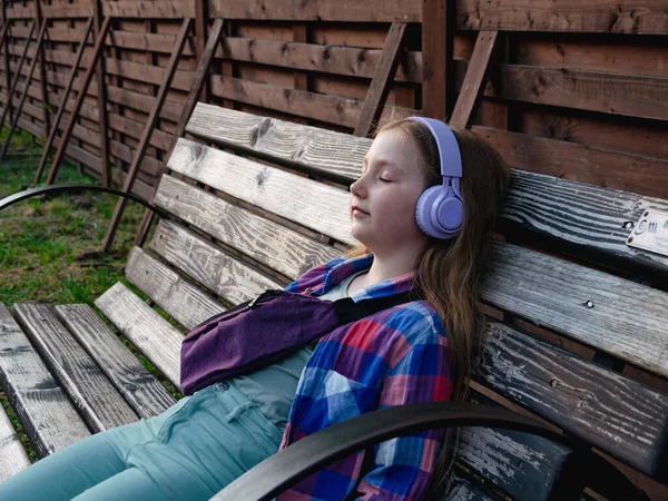 stock image Blonde child purple headphones listen to meditation music podcast smartphone bench outside city street urban lifestyle.Concentrated young girl online audio book Mental health Stress relief digital app