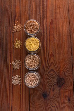 Tahta arka planda cam kavanozlardaki tahıl taneleri. Farklı Groats koleksiyonları. Arpa, yulaf, darı ve buğday. Yüksek lif içerikli kepekli gıdalar düz yerde yatıyordu. Sağlıklı beslenme malzemeleri.