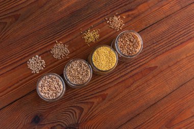 Tahta arka planda cam kavanozlardaki tahıl taneleri. Farklı Groats koleksiyonları. Arpa, yulaf, darı ve buğday. Yüksek lif içerikli kepekli gıdalar düz yerde yatıyordu. Sağlıklı beslenme malzemeleri.