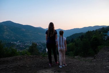 Gezginler anne ve kızı geride durup güzel Karpat Dağları 'nın arka planında gün batımında doğanın tadını çıkarırken eğleniyorlar. Aktif yaşam tarzı aile turizmi konsepti.