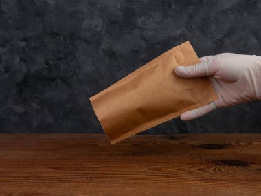 Çanta maketi. Koruyucu eldivenler içinde kahve çekirdeği ahşap arkaplanlı kahverengi kraft kağıt paketi var. Toka şablonlu ambalaj yiyecek teslimatı çay ağırlıklı ürün bırakır. Mağaza satış reklam tasarımı