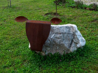 İnek bahçesi heykelleri, süt çiftliği çevre dostu taşlar ve yeşil çimlerde demir heykeller. Peyzaj tasarımı ev dekorasyonu aksesuarları. Doğal malzemelerden kırsal dekor - kayalar, demir, tel