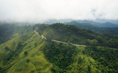 Hava aracı Tayland 'daki yeşil ormandan ve dağdan geçerek kırsal yolda uçuyor. Dağ kıvrımlı zig zag yolu. Üst hava görüntüsü