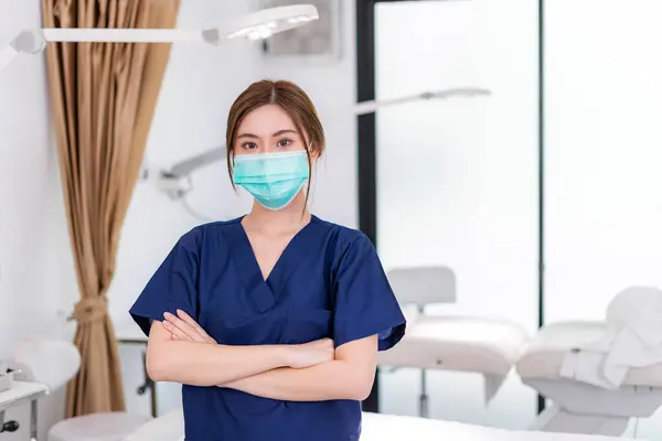Beauty clinic and health concept. Confident woman physician Wearing protective medical mask and crossing arms on her chest posing and smile friendly with copy space for your advertising information.