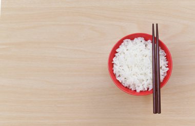 Kırmızı seramik kâse çubuklarıyla haşlanmış pirinç ve ahşap arka planda. Asya yemekleri. Üst görünüm.