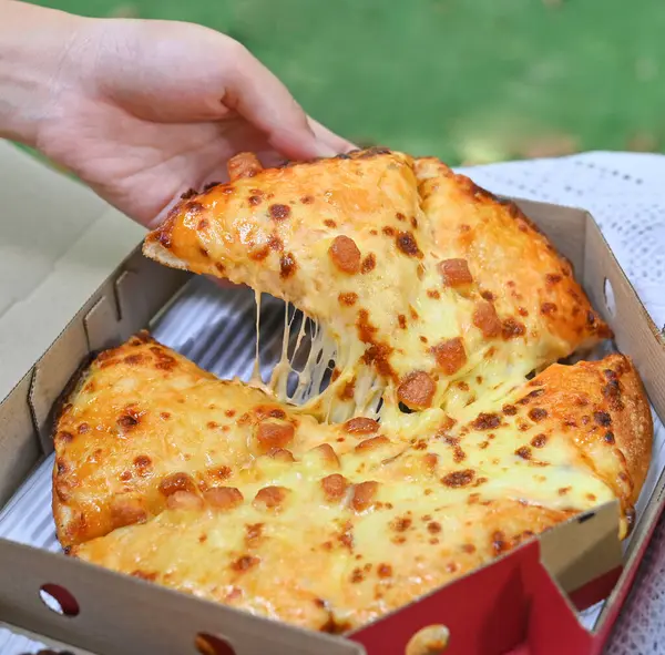 Hand picks up a slice of pizza with stretched cheese isolated on box background.
