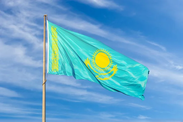 The flag of the Republic of Kazakhstan flutters in the wind against a blue sky with a little cloudiness. State symbol of Kazakhstan.