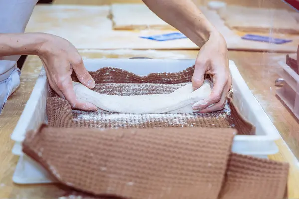 The process of baking baguettes in a bakery or restaurant. The bakers hands shape and place the dough for baking baguettes on a fabric backing.