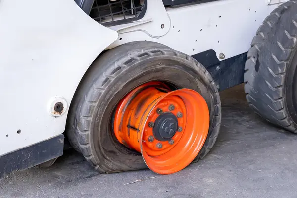 Close-up view of a flat or torn tire on a compact forklift or compact loader. A broken car is waiting for repair in a car repair shop. Malfunction of municipal equipment.