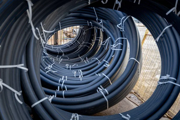 Coils of black polyethylene pipes for laying high voltage electrical cables underground at a construction site. Electrical insulation.