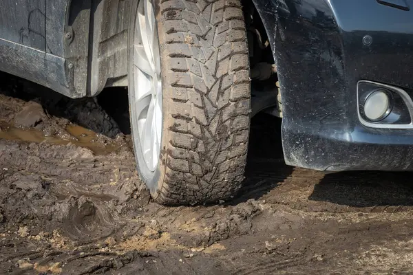 Winter car tires are covered with mud, the car is in the mud. Tough road conditions highlight the need to use the right tires to drive safely in challenging conditions.