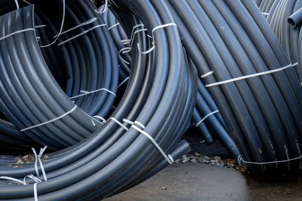 Several rolled up small diameter polyethylene pipes for laying high voltage electric cables underground. Warehouse or construction site or storage. Black pipes coiled into rings or spool or coils.