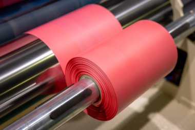 Roll of red polyethylene film for bags and packaging. Extrusion line for the production of polyethylene film for products packaging. Winding a polyethylene roll for packaging. clipart
