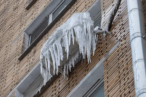 Icicles hang from an air conditioning unit on a brick building. Frozen Air Conditioning Unit with Icicles.