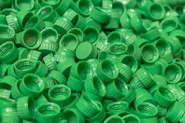 Industrial production of bottle caps made of green high-density polyethylene. A pile of freshly molded green HDPE plastic bottle caps. Production of food packaging.