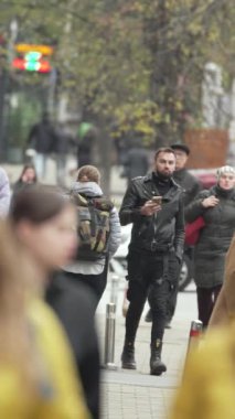 KYIV, UKRAINE - 6 Ekim 2024: Sonbaharda sokakta yürüyen insanların dikey videosu, yavaş çekim